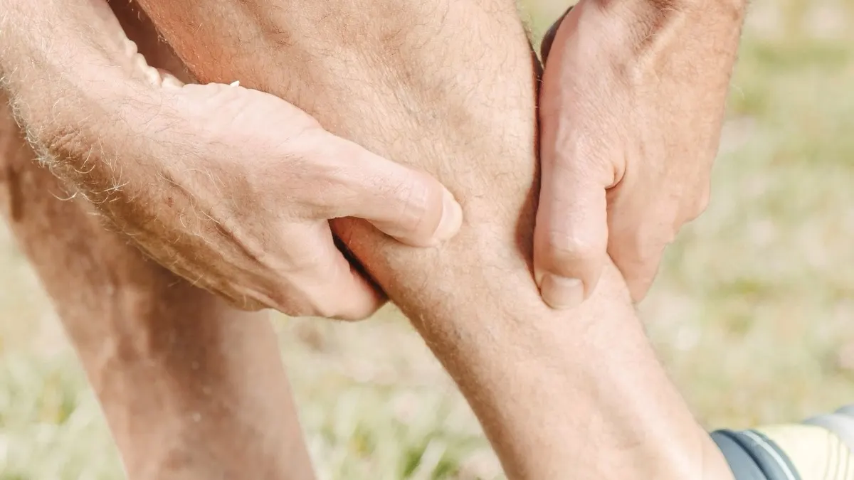 A man's hands gripping and rubbing his bare calf outdoors