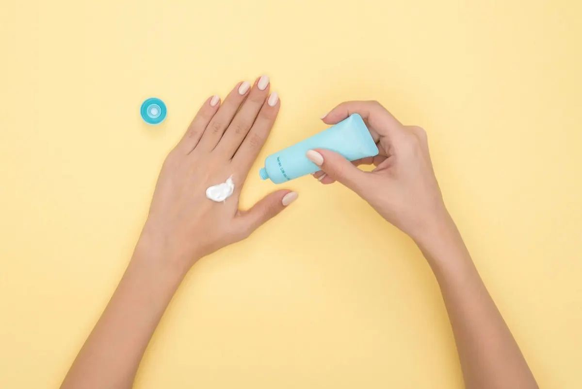 Top-down view of a hand with a dab of white cream, the other hand holding a blue tube