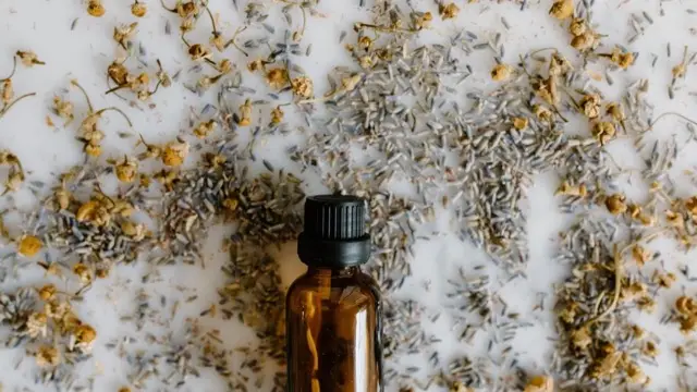 Brown glass dropper bottle surrounded by scattered dried lavender and chamomile flowers on a white surface