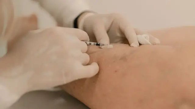 Gloved hands guiding a fine syringe into the skin of a leg during an injection procedure