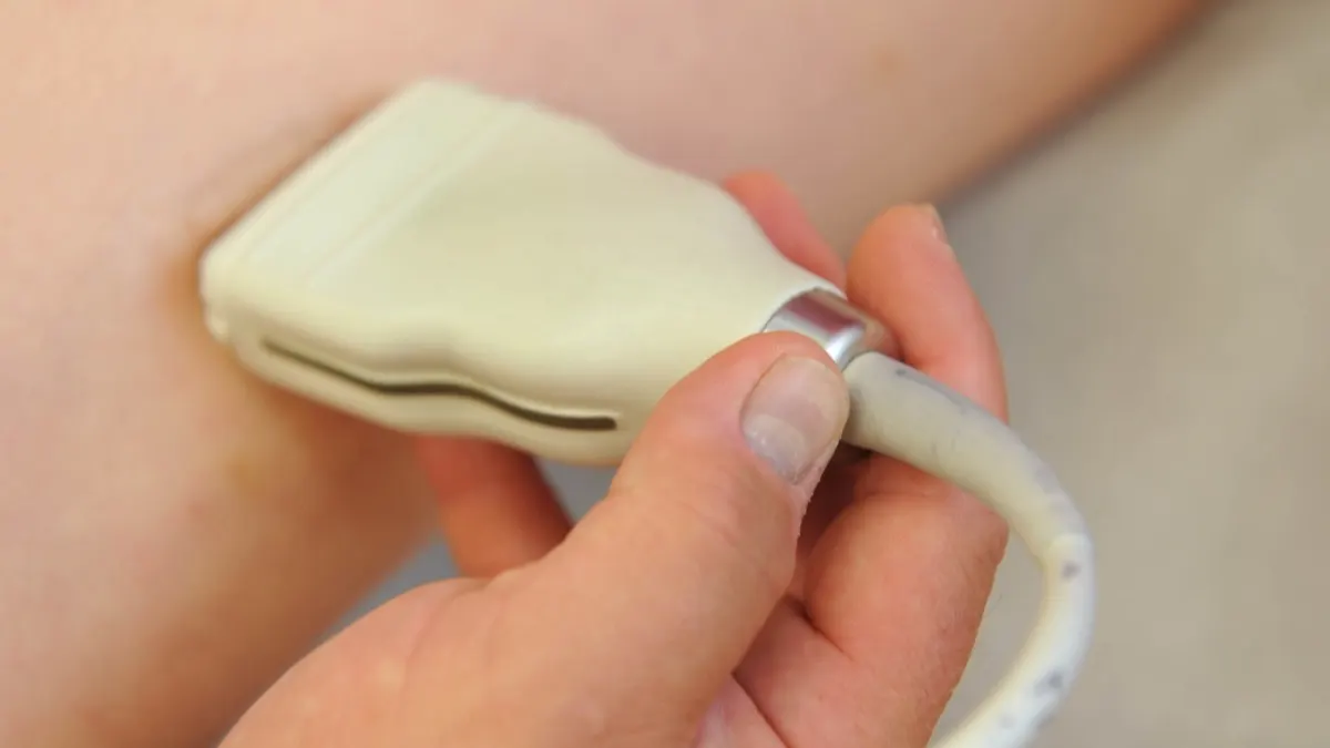 Close-up of a hand holding a handheld ultrasound probe against the back of a leg during a vein examination