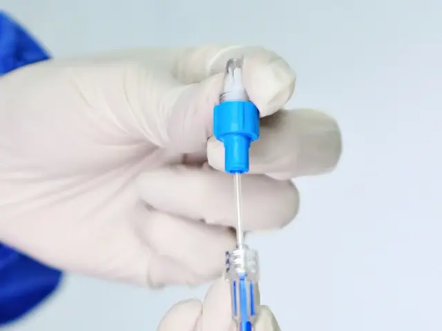 Gloved hand holding a thin medical catheter with a blue connector hub against a pale background